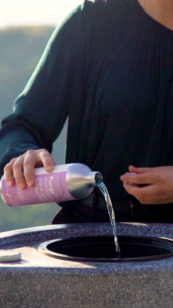 Person pouring liquid from a bottle into a hot tub with a scenic background