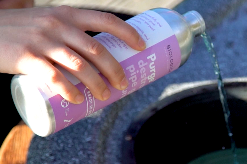 Person pouring a liquid from a bottle into a stone sink outdoors.