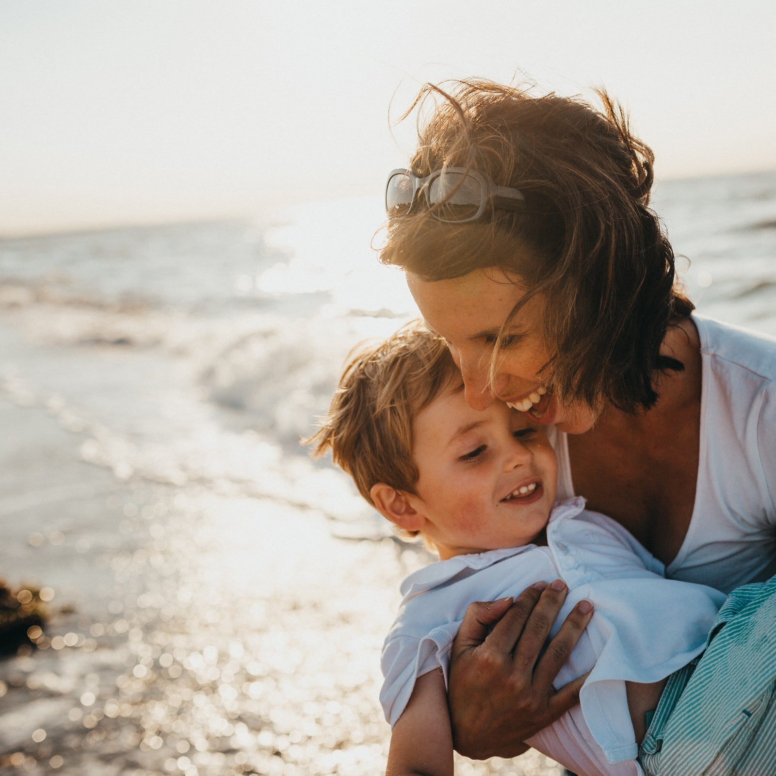 A young smiling mother, carrying her son over waves on a sunny beach
